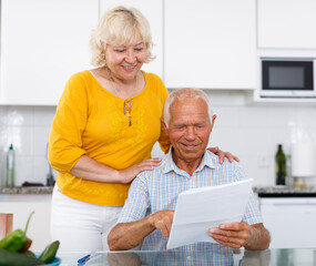 Portrait of mature family couple with bills at kitchen table in home