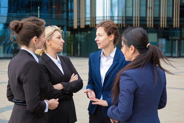 Serious confident business ladies discussing contract outdoors. Businesswomen wearing suits standing together in city and talking. Cooperation and teamwork concept