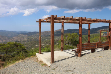 A bench for rest with a sunshade in the Troodos mountains against a blue sky with clouds. Cyprus.