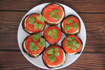 Eggplant appetizer with tomato and mayonnaise on a white plate and a background of fresh tomatoes