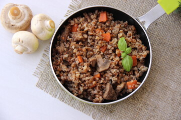 Buckwheat with meat and mushrooms in a pan, next to mushrooms, top view