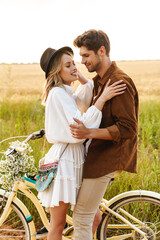 Image of young couple hugging while riding bicycle in countryside