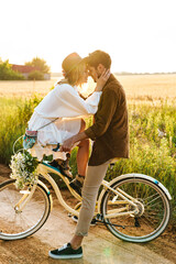 Fototapeta premium Image of young couple kissing while riding bicycle in countryside