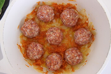 Raw minced meat meatballs with rice and carrots in a pan with vegetables
