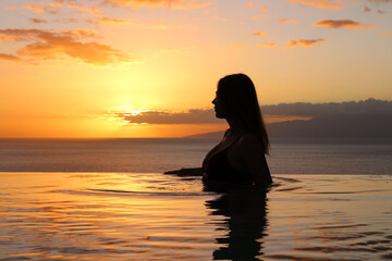 Fototapeta premium A girl in a swimsuit with her hair down stands sideways and looks at the sunset.