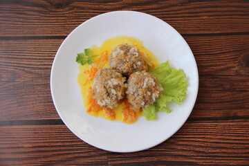 Meatballs with rice and carrots on a white plate and dark wooden boards