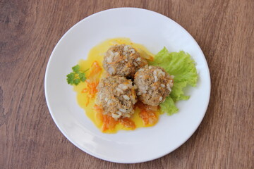 Meatballs with rice and carrots on a white plate and dark wooden boards