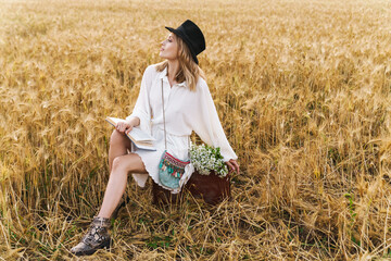 Image of young blond woman reading book while sitting in golden field