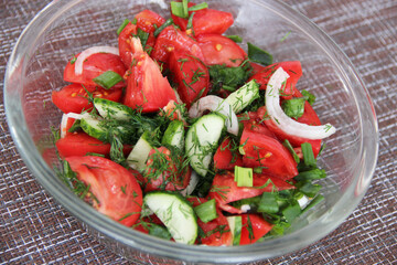 Homemade salad of fresh cucumbers and tomatoes with onions and herbs in a transparent Cup