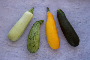 several types mixed yellow, white, stripped and green zucchini's on a grey concrete background. top view, copy space