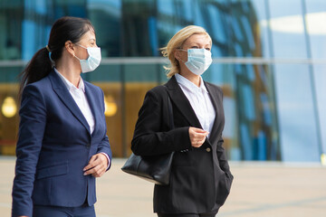 Business colleagues wearing office suits and masks, meeting and walking together in city, talking,...