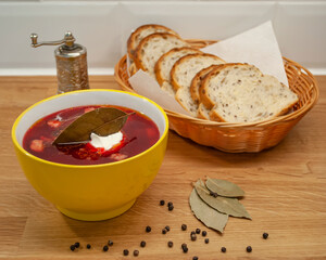 Delicious fresh borscht on meat cooked at home. A plate of soup and sliced bread on a wooden table....