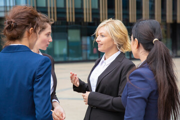Female business partners discussing deal outdoors. Businesswomen wearing suits standing together in city and talking. Corporate communication concept