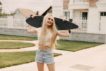 Teenage girl wearing denim shorts and white t shirt holding a long board, standing on street in the neighborhood.