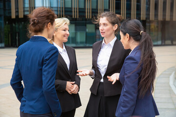 Female business group meeting outdoors and talking. Businesswomen wearing suits standing together in city. Corporate discussion and teamwork concept