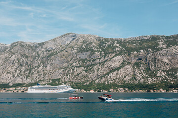 Fototapeta na wymiar White cruise multi-storey liner against the background of the mountain. Two motor boats are sailing on top of each other.