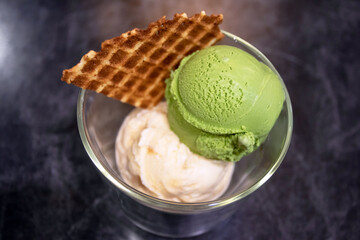 Green tea matcha and salt caramel ice cream scoop in glass on a grey stone background. Top view and copy space.