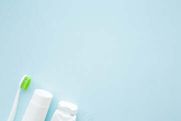 Fototapeta na wymiar White tube of toothpaste, toothbrush with green bristles and container of dental floss on pastel blue background. People teeth hygiene concept. Empty place for text or logo. Closeup. Top down view.