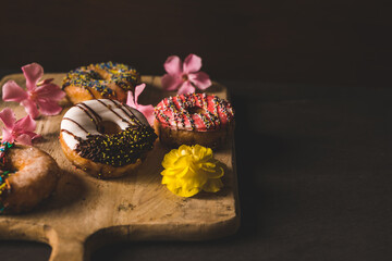 still life colorful donuts on a wooden table with some flowers