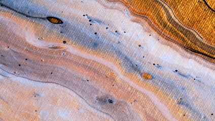Close up of an acrylic pouring artwork on canvas, resembling a beach scene with natural swirls and curvy diagonal lines. Golden sand with light reflections, and a visible canvas texture.
