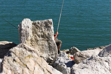 A fisherman is fishing with two fishing poles behind a rock (Pesaro, Italy, Europe)