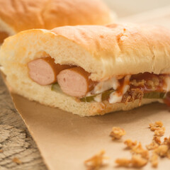 Close up of fresh hot dog with two sausages and sauce, with fried onion and cucumber.