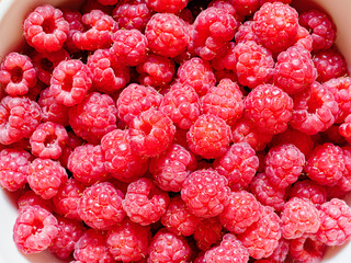 Juicy and ripe fresh raspberries are in a white bowl. Natural berry background.