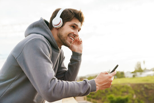 Image of joyful sportsman using headphones and cellphone