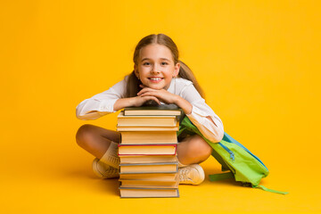 Little Schoolgirl Smiling Sitting At Stack Of Books, Yellow Background