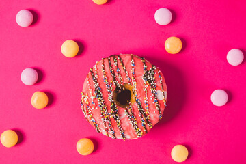close up of a pink donut on a pink background with colorful candies 