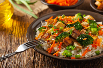 Tofu with rice and vegetables. Served on brown plate.