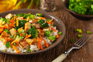 Tofu with rice and vegetables. Served on brown plate.
