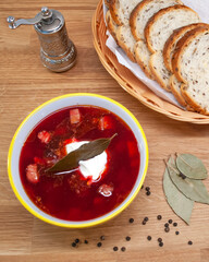 Delicious fresh borscht on meat cooked at home. A plate of soup and sliced bread on a wooden table. Cooking at home during isolation. Working and cooking at the same time at home.