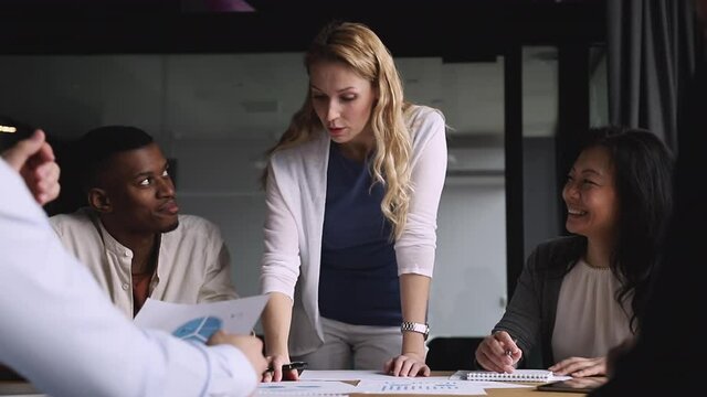 Skilled businesswoman boss leader analyze business documents teach diverse workers explain project plan review financial data paperwork at group meeting training team at corporate office briefing