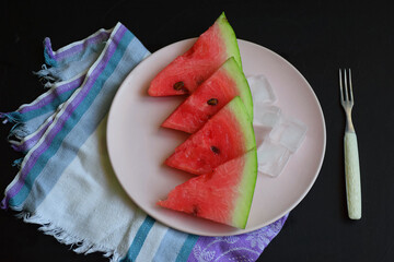 Slices of ripe watermelon on a light plate on a dark background