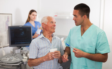 Man doctor and elderly man patient before ultrasound diagnostic, woman on background