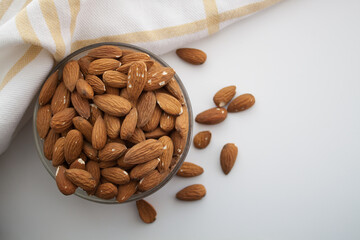 Almond in a bowl and kithen towel in the left side of white background
