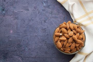 Almond in a bowl and kitchen towel in the right side of violet grunge background
