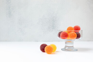 Colored balls of fruit marmalade in a transparent glass bowl on a light scuffed background. front...