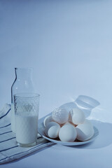 Milk in glass and eggs with long shadows toned in blue. Vertical orientation with copy space