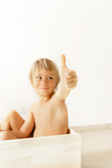 Blonde baby boy in a wooden box on a white background. Show sight thumb up. Selected focus. 
