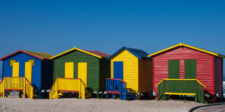 Colorful wooden huts on Muizenberg beach under a clear blue sky in Cape Town, South Africa