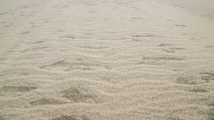 Small dunes of gray-beige grainy sand waves going into perspective, the surface is covered with ripples on the beach of the sea coast. Natural mineral sand background