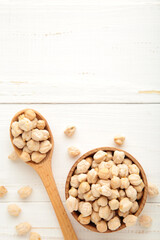 Uncooked chickpeas in wooden spoon and bowl on white background