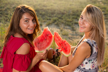 two girls on a picnic, holding large slices of watermelon in their hands and laughing, one girl with braces on her teeth