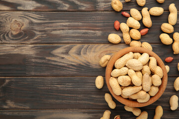 Dried peanuts in wooden bowl on brown wooden background.