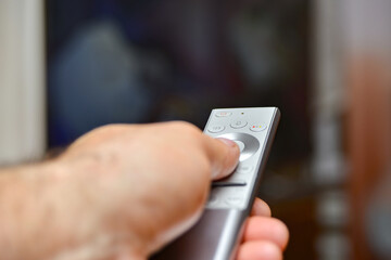 A man holds a remote control in his hand and switches channels to watch TV. Remote control of household appliances.