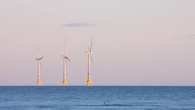 Three offshore wind turbines at sunset off the UK coast