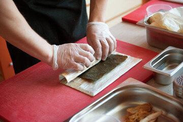 Roll sushi on a bamboo rug with your hands on the table.