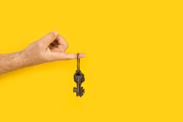 La mano de un hombre sosteniendo un manojo de llaves sobre un fondo amarillo brillante liso y...